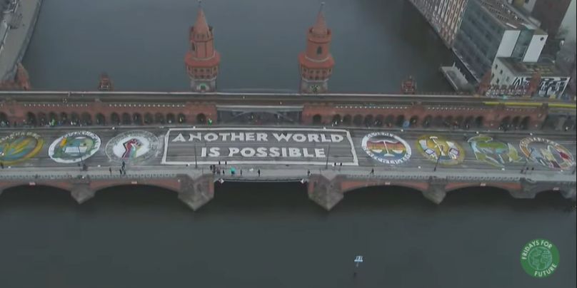 Screenshot Brücke mit Spruch Another world is possible und Logos