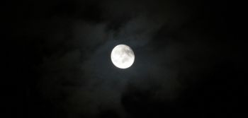 Mond hinter Wolken vor schwarzem Himmel